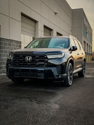 Black Honda Pilot Black Edition SUV parked in front of industrial warehouse building.