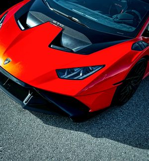 Red Lamborghini Huracan STO supercar front hood and headlights close-up on asphalt track.
