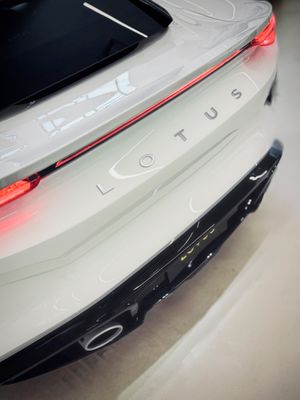 Close-up rear view of a white Lotus sports car showing the brand logo, red tail lights, and black diffuser.