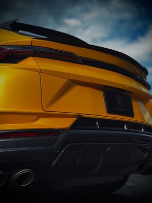Close-up rear view of yellow Lamborghini Urus SUV with carbon fiber diffuser under cloudy sky.