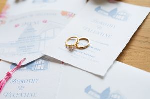Gold wedding rings rest on elegant blue and white illustrated wedding invitations for Dorothy and Valentine.
