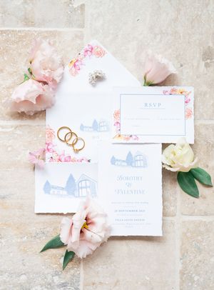 Wedding invitation suite with pink floral envelope, gold rings and blush peonies on stone.