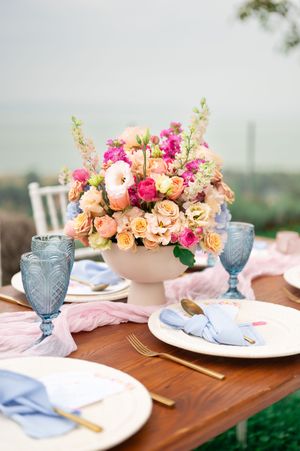 Elegant wedding table with pink and peach floral centerpiece, blue glassware and gold cutlery.