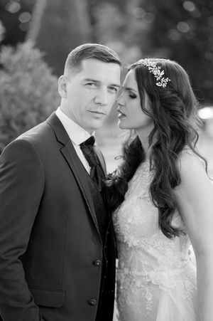 Intimate black and white portrait of bride and groom close together outdoors, bride wearing floral hair accessory.