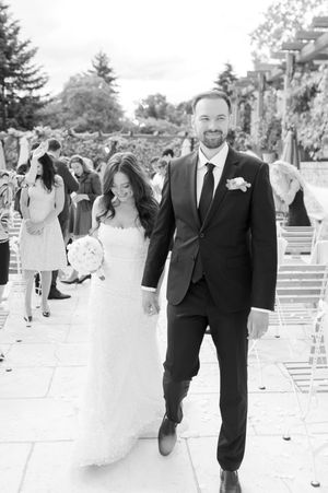 Black and white photo of smiling newlyweds walking hand in hand down the aisle after ceremony.