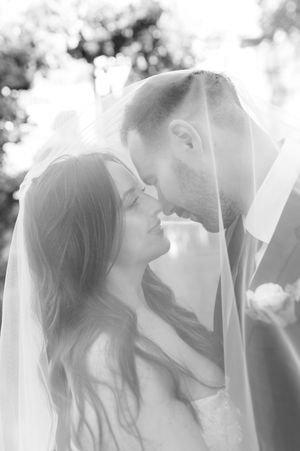Black and white romantic portrait of bride and groom sharing tender moment under bridal veil.