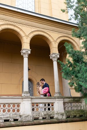 Couple shares romantic kiss on ornate balcony of yellow historic building with arched columns.