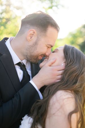 Groom tenderly holds bride's face as they share an intimate almost-kiss moment outdoors on their wedding day.