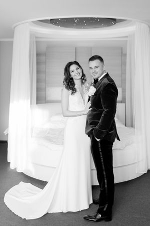 Black and white portrait of elegant bride and groom posing together in front of a canopy bed in a luxury suite.