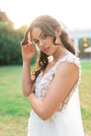 Stunning bride in lace applique wedding dress poses at golden hour with soft glowing backdrop.