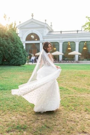 Bride in flowing white gown with veil twirling at golden hour outside elegant white venue.