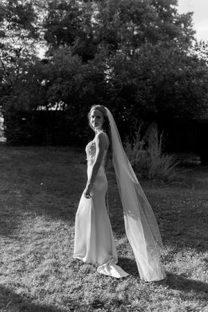 Elegant bride in fitted gown with long cathedral veil poses in black and white garden portrait.