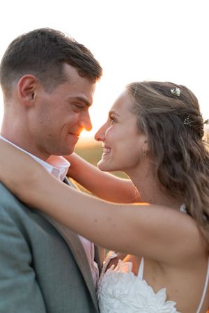Bride and groom share an intimate golden hour moment, smiling at each other in warm sunset light.
