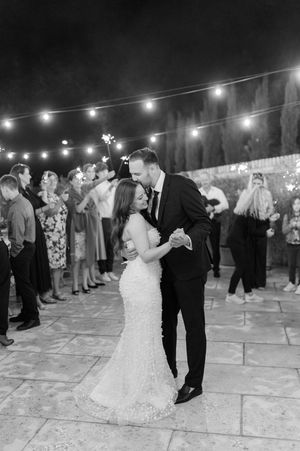 Bride and groom share romantic first dance under string lights while guests hold sparklers at night.