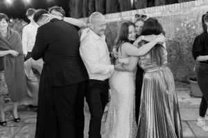 Black and white photo of wedding guests sharing warm embraces on the dance floor at reception.