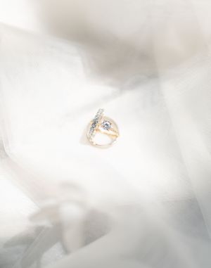 Elegant gold diamond engagement ring resting on soft white bridal veil fabric.