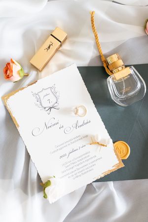 Wedding invitation for Noemi and Andras with gold details, perfume, and roses on white silk.