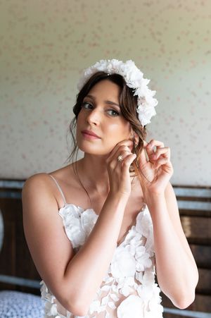 Beautiful bride in floral white gown adjusting her earring with a flower crown in her hair.