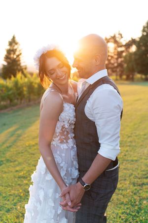 Bride and groom share a romantic sunset moment in a vineyard, holding hands and smiling.