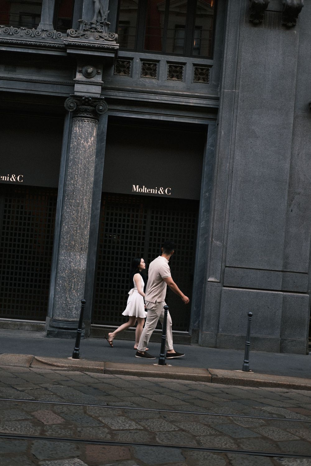 Couple walking past Molteni & C luxury furniture store on a cobblestone street in Milan, Italy.