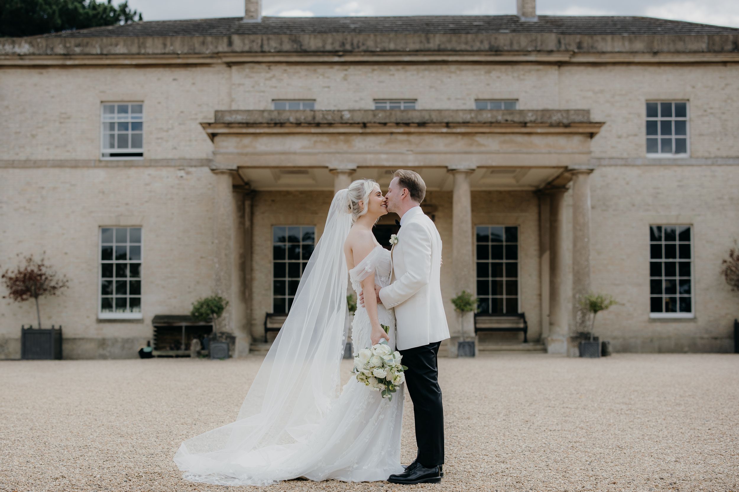 Bride and groom share a romantic moment outside an elegant Georgian manor house, bride wearing a flowing veil.