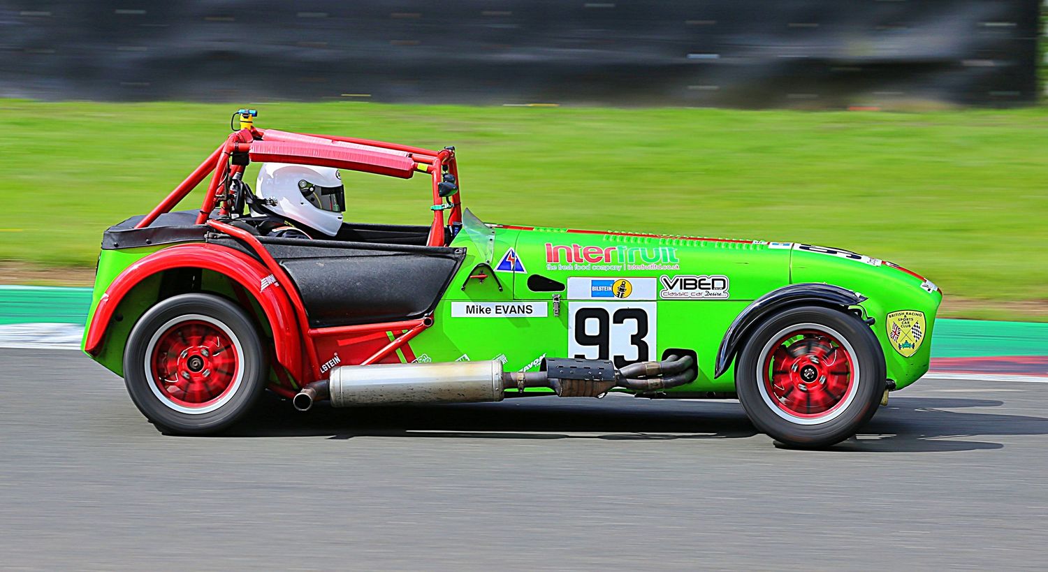 Green and red vintage racing car number 93 speeding on a race track circuit.