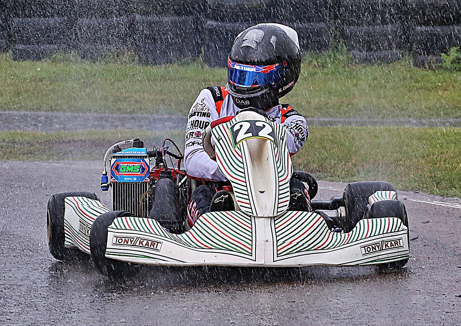 Go-kart racer driving a Tonykart in wet rainy conditions on a motorsport circuit.