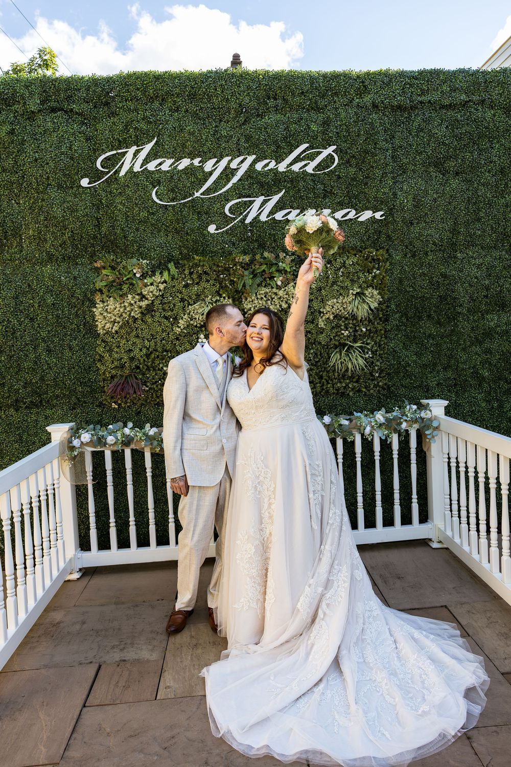 Bride and groom celebrate at Marygold Manor wedding venue, posing in front of lush green hedge backdrop.