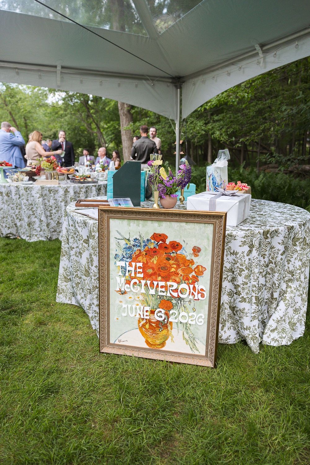 Outdoor wedding reception with a framed floral sign reading The McGiverons June 6, 2020 on grass under a white tent.