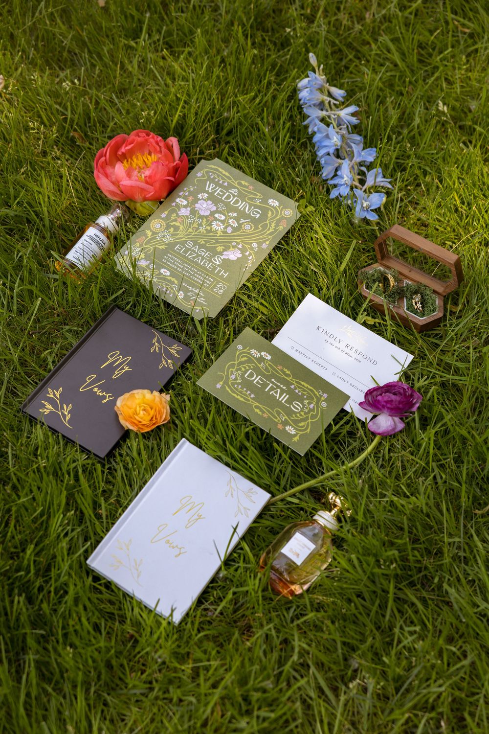 Wedding stationery suite with floral invitations, details card, and vow books arranged on green grass with flowers.