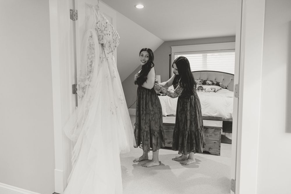 Two bridesmaids in floral dresses admire a wedding gown hanging in a bright bridal suite.