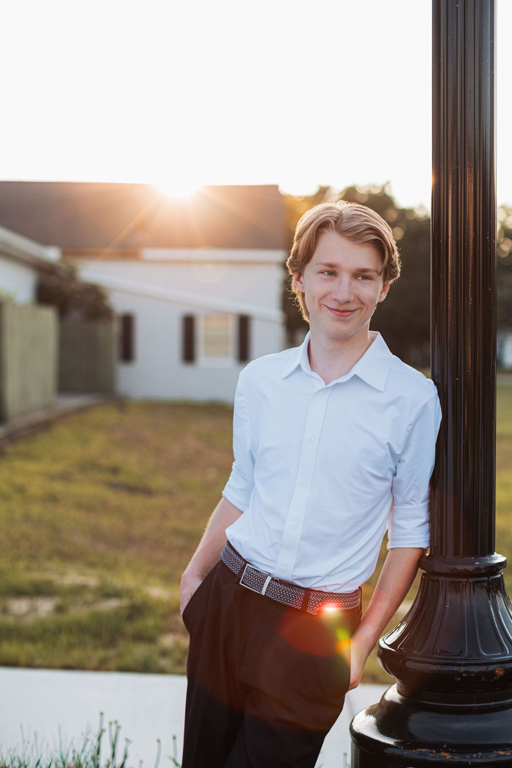 Senior boy photo in Howell, MI; boy standing in against light post downtown at golden hour with sun flare, by South Lyon photographer