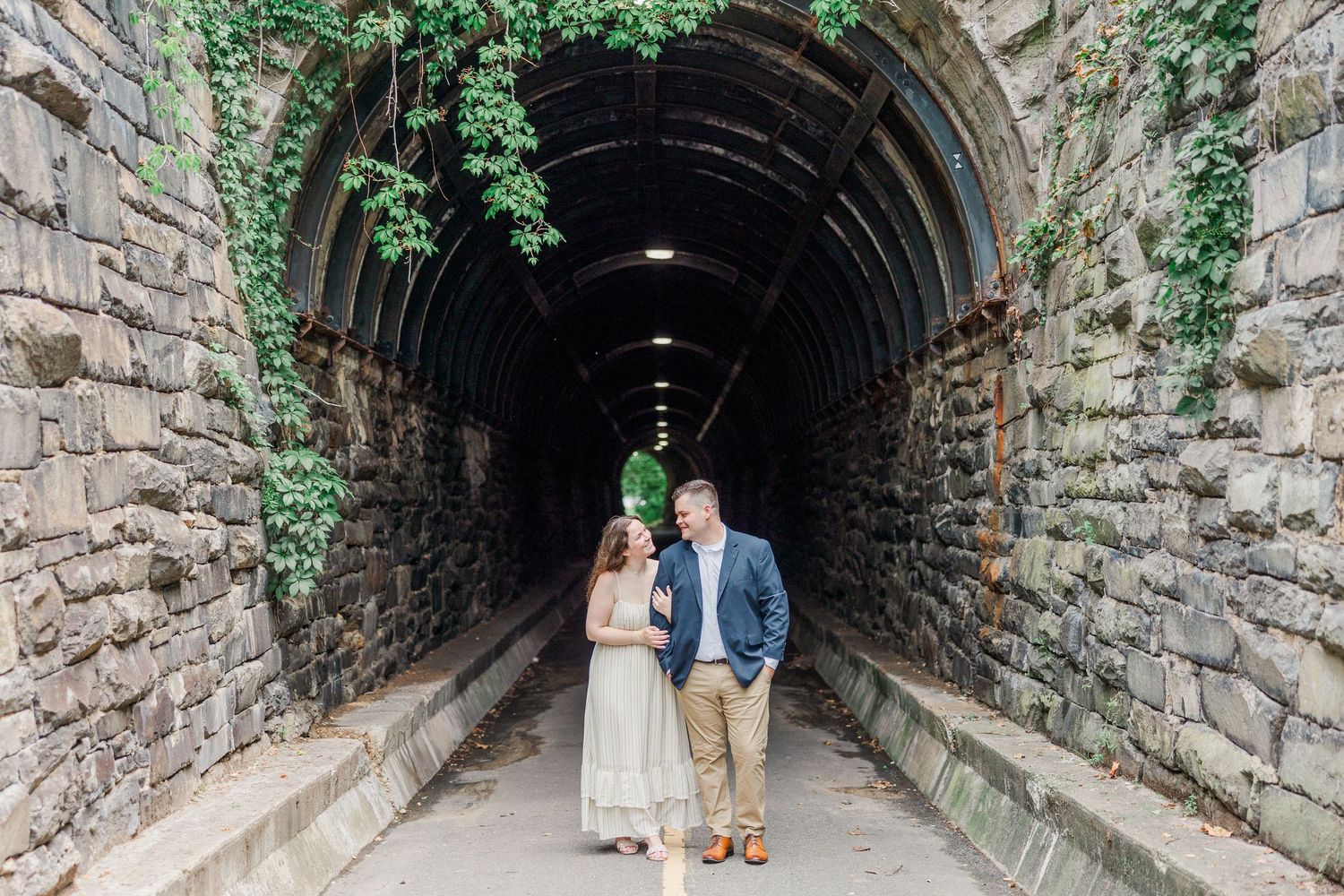 Couple standing together in a stone tunnel archway covered in ivy, sharing a romantic moment during an engagement photo session.