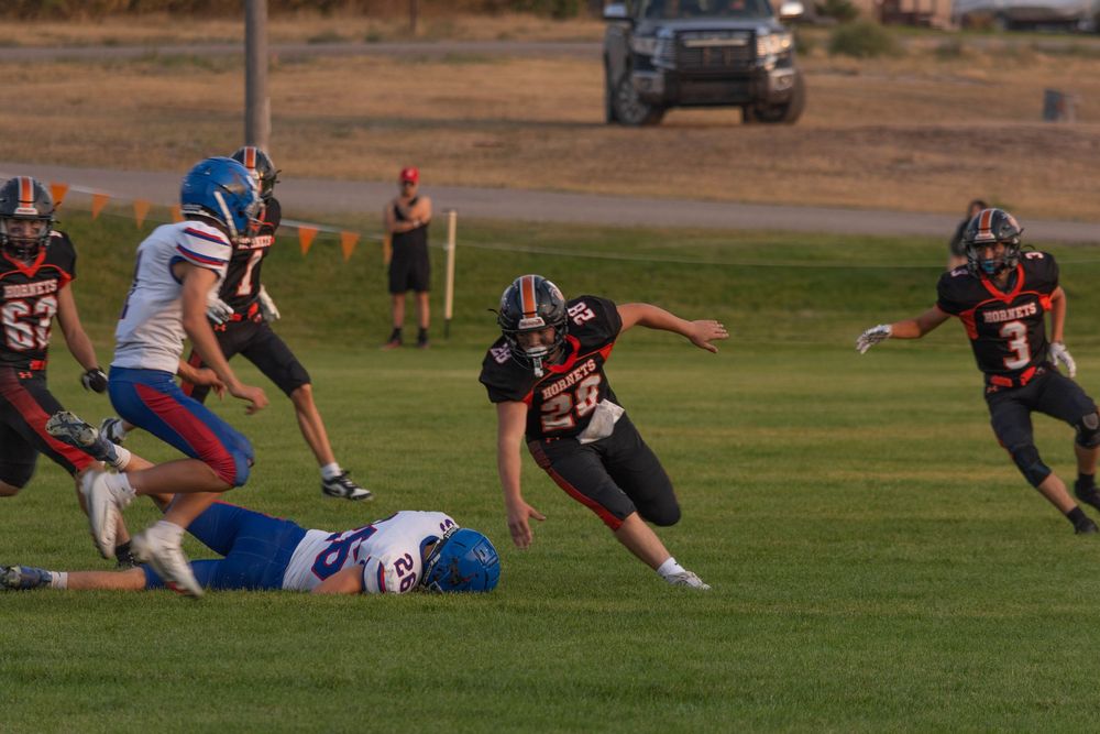 Youth football players compete in a game, with players in black and white uniforms tackling opponents in blue on a green field.