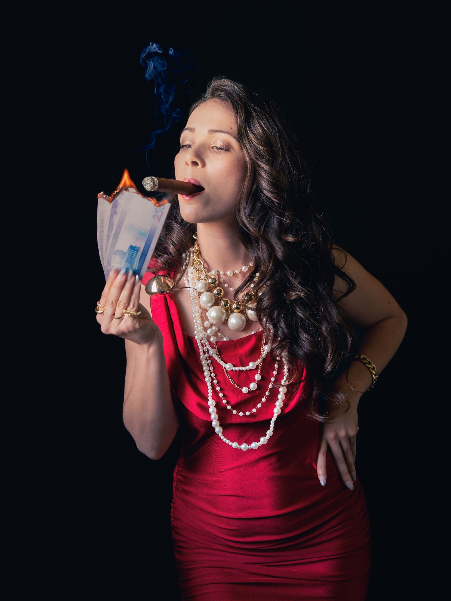 Woman in red dress smoking cigar, burning money, wearing pearl necklace and feathered headpiece on black background.