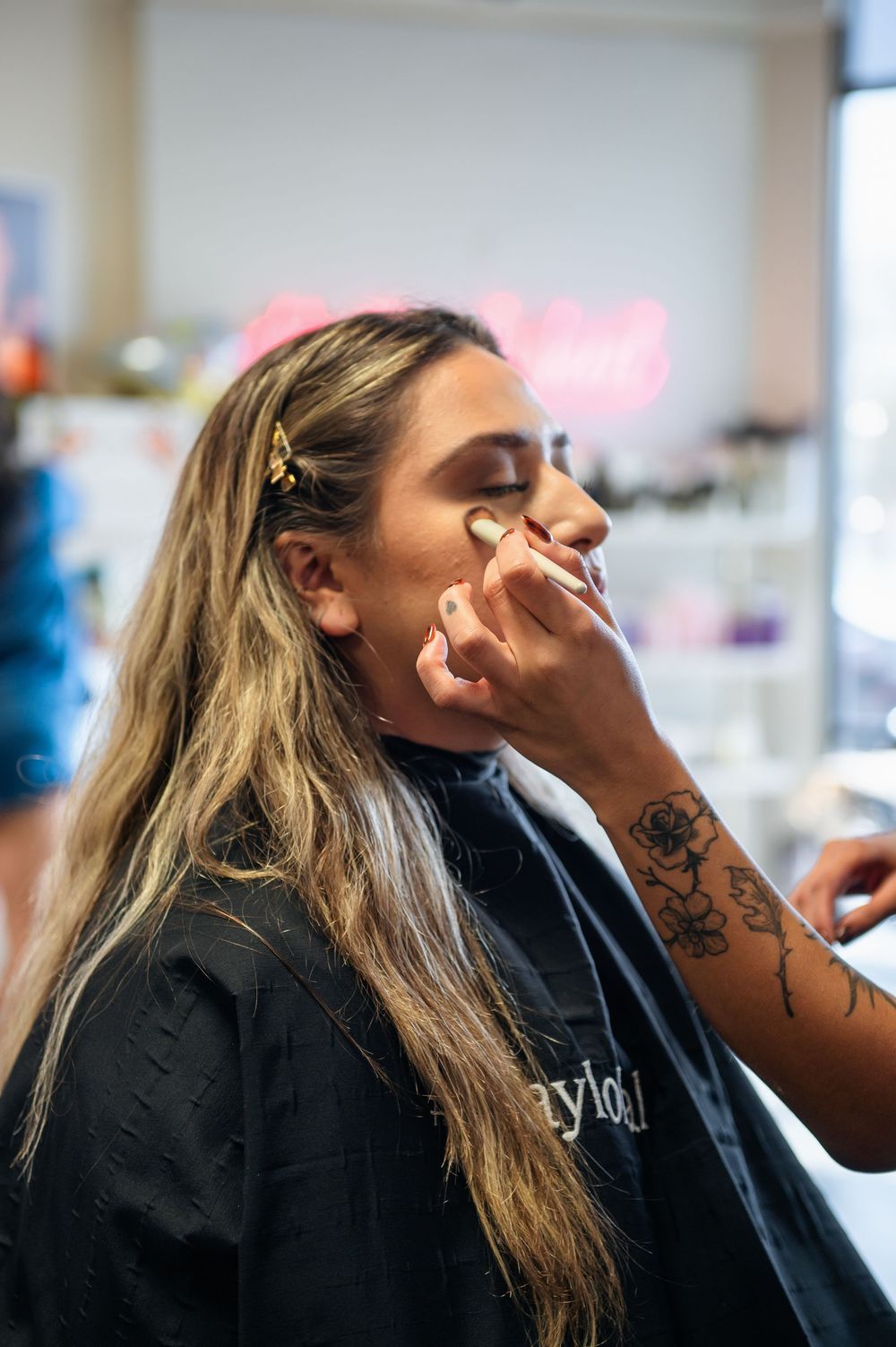 Bride getting professional makeup applied at a salon while wearing a black cape before her wedding.