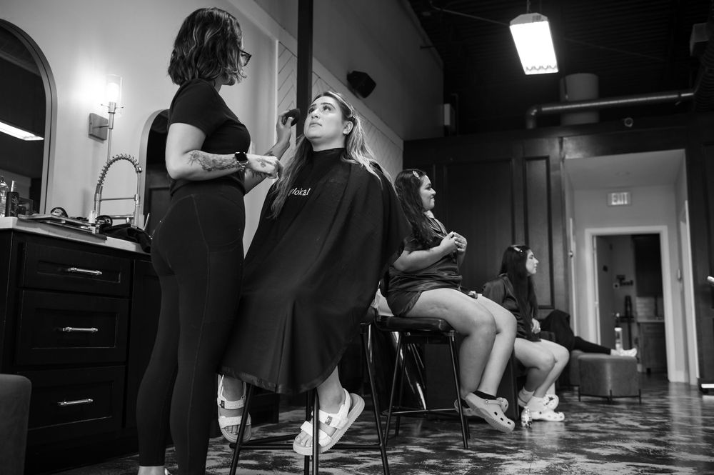 Bride getting hair styled by stylist in salon chair, black and white photo.