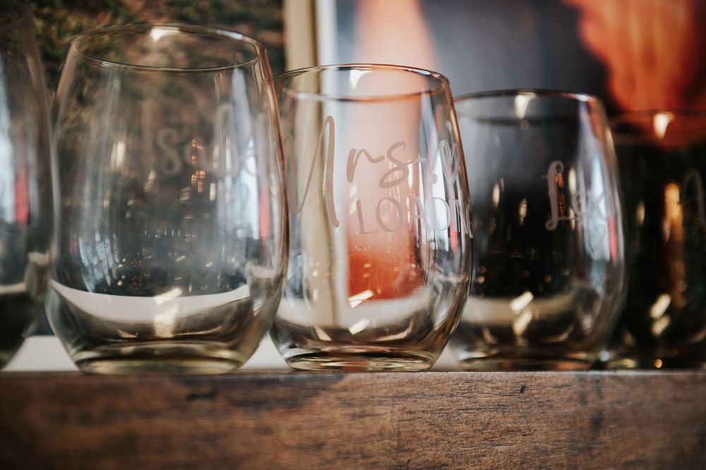 Personalized etched stemless wine glasses displayed on a rustic wooden shelf.