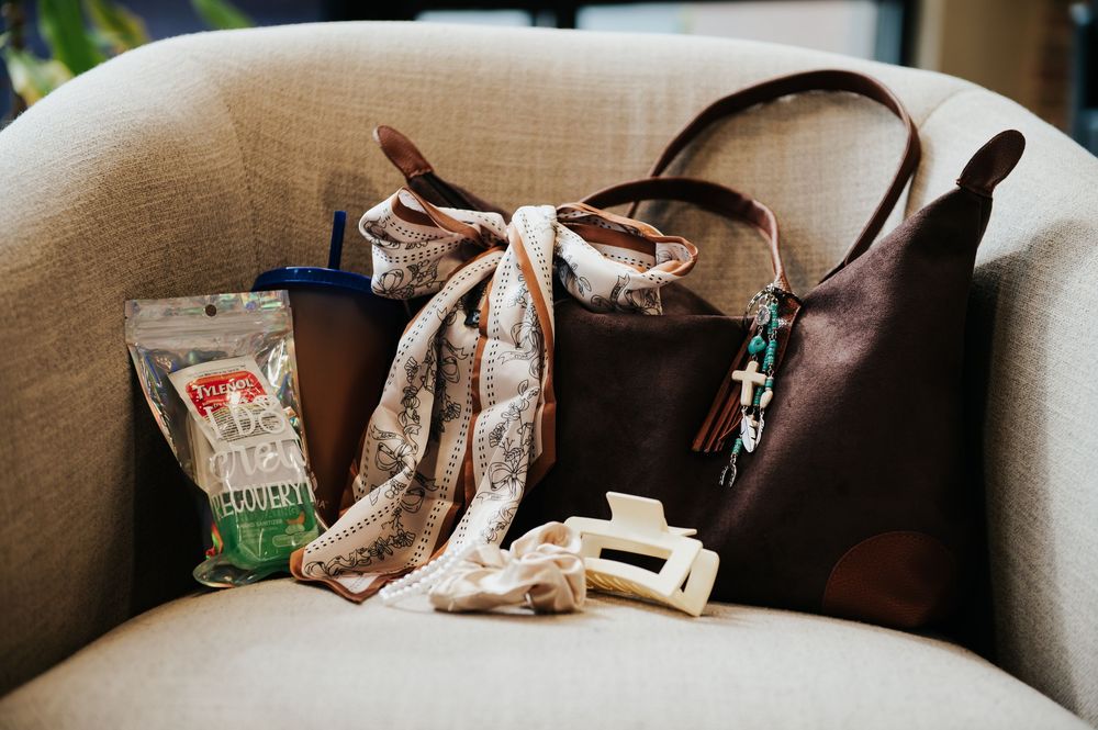 Brown leather tote bag with floral scarf and snacks on neutral chair.