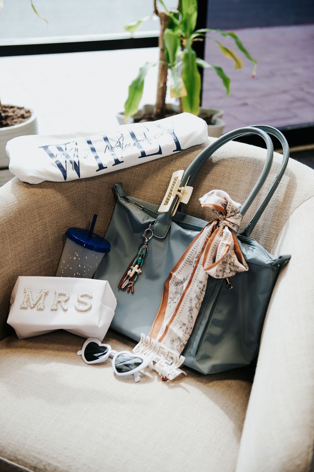 Bridal gift set with MRS pouch, tote bag, heart sunglasses, and WIFEY pillow on a chair.