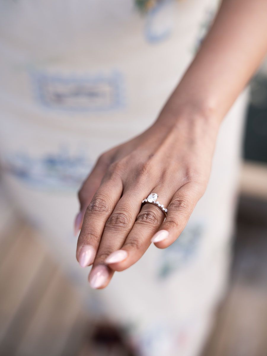 Close-up of a woman's hand wearing a stunning diamond engagement ring with a floral band, paired with light pink nails.