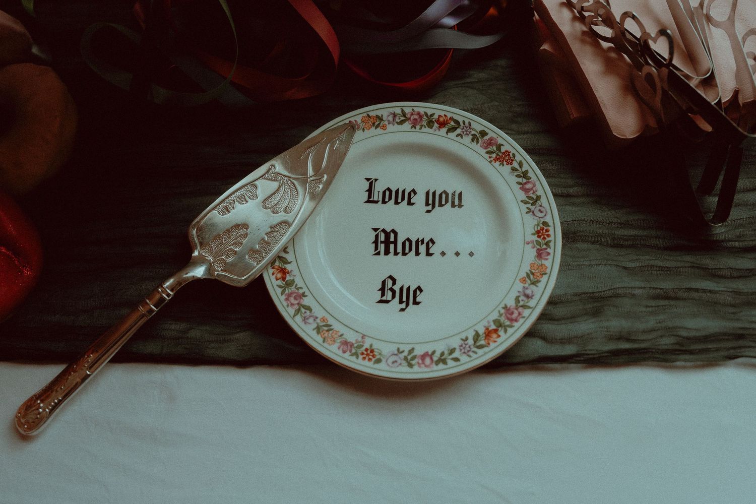 Decorative plate with "Love you More... Bye" text and floral border, displayed with a vintage silver cake server.