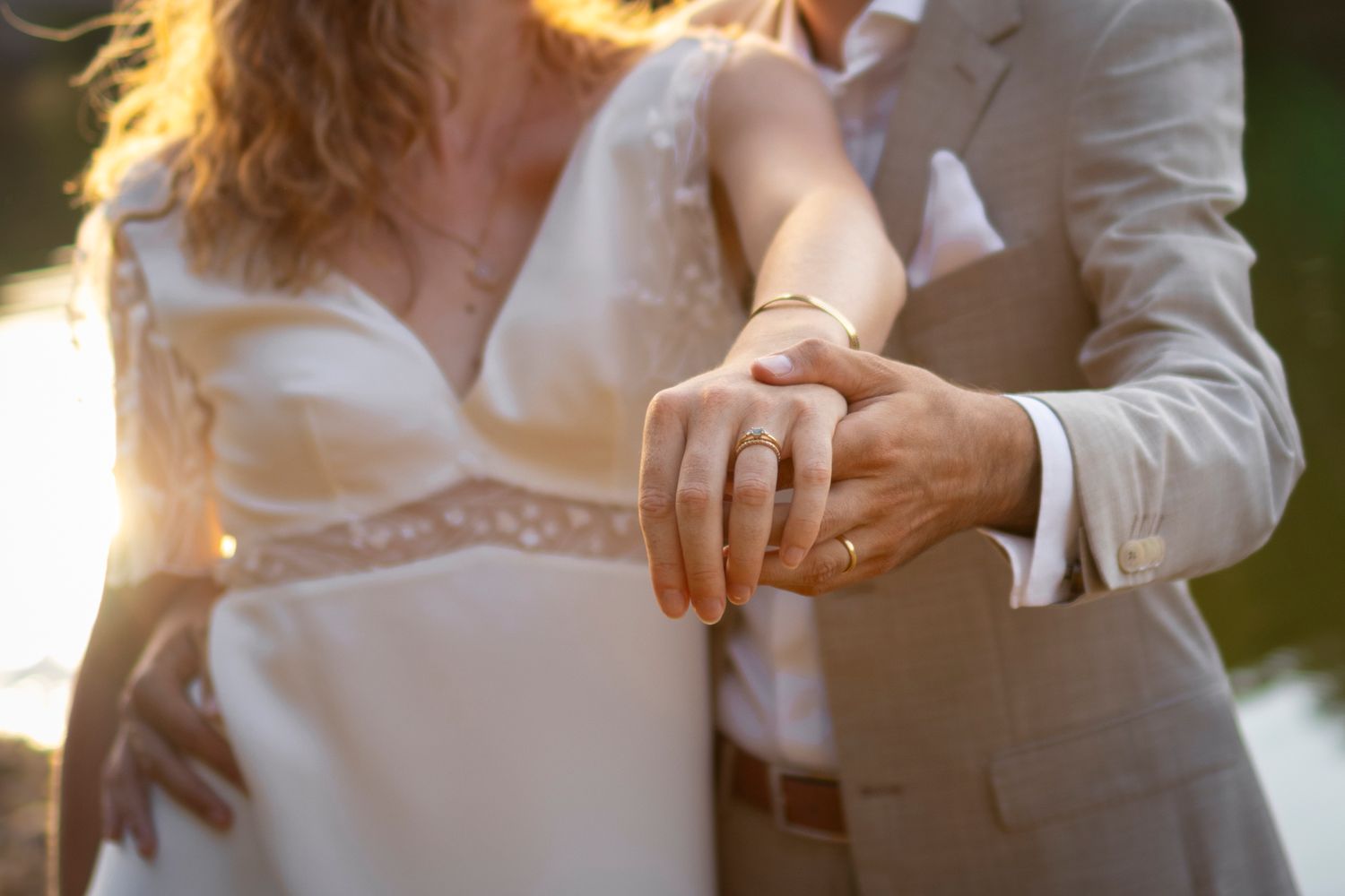 Gros plan sur les mains et les alliances d’un couple de mariés dans une lumière dorée, Lyon