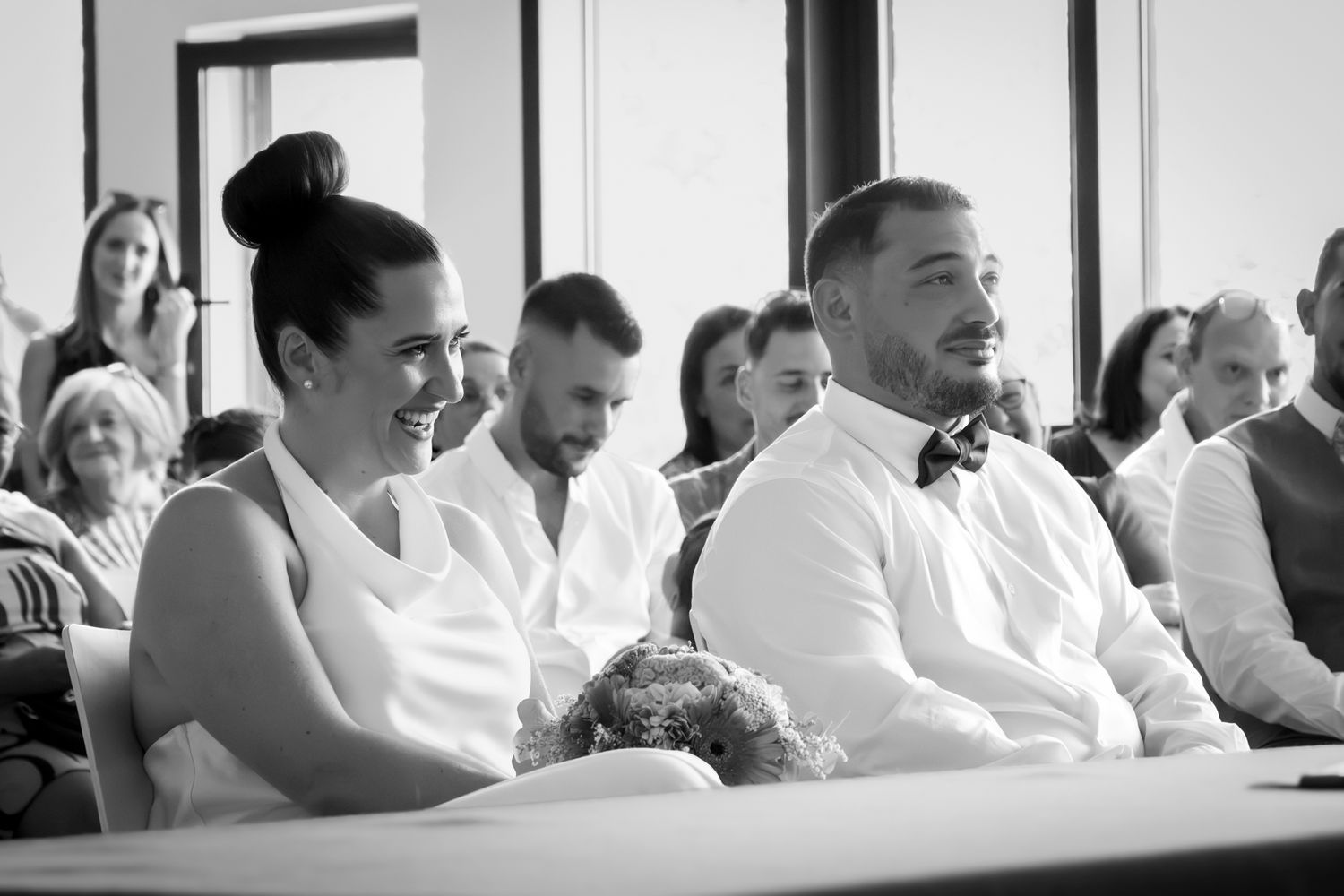 Mariés souriants assis devant leurs invités pendant la cérémonie civile, noir et blanc, Lyon
