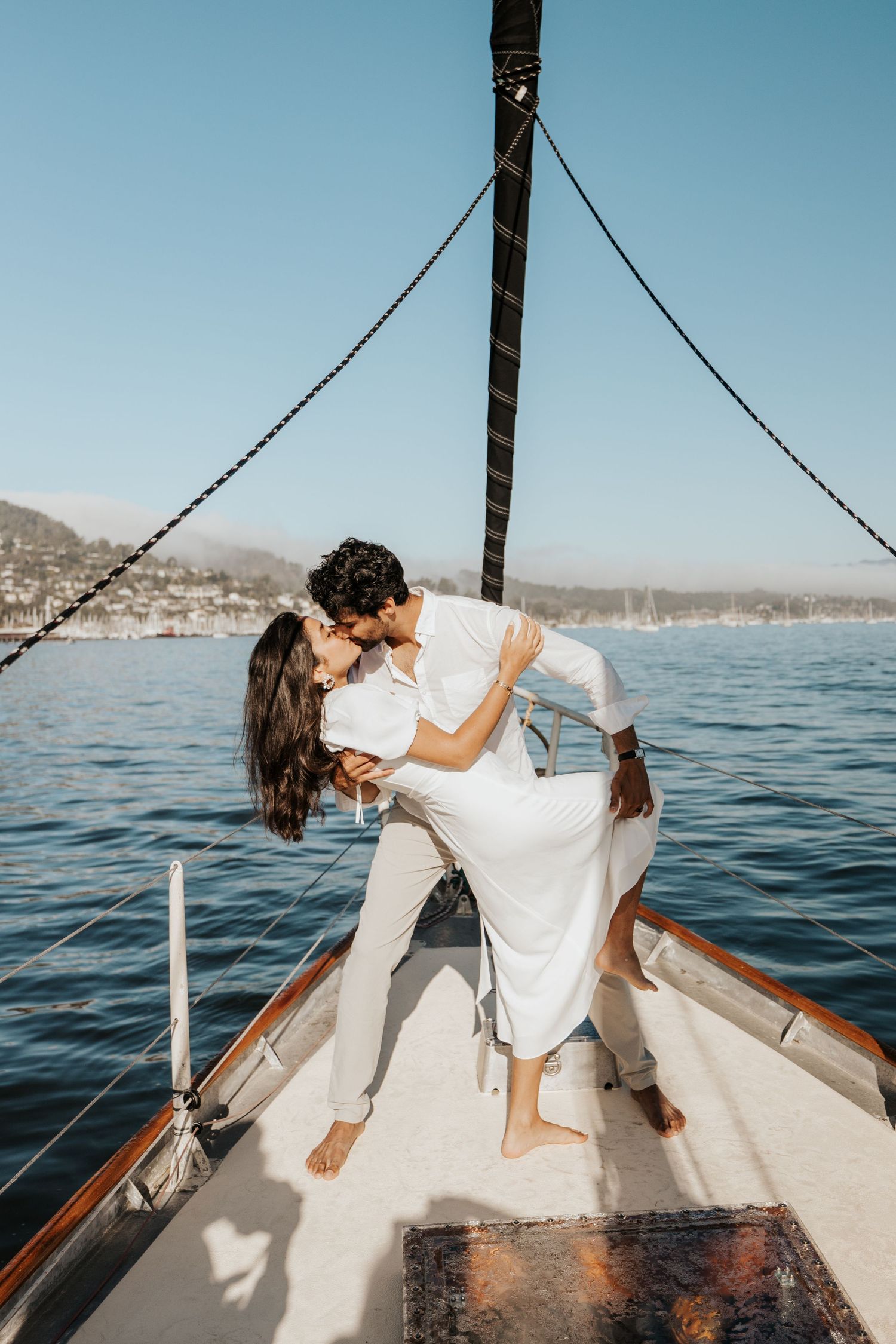 couple dip kissing on bow of sailboat in the san francisco bay off of sausalito