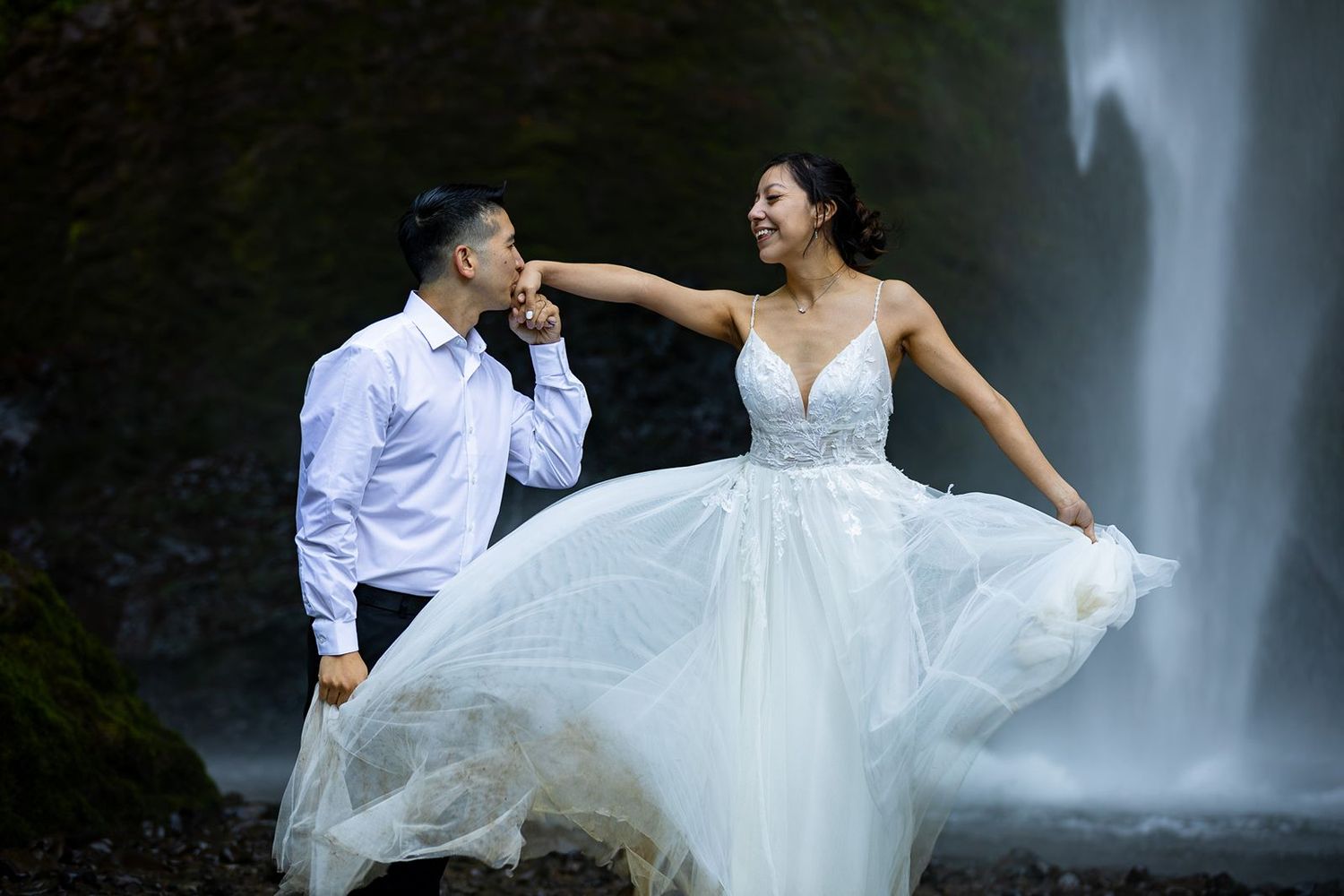 Couple in wedding attire poses romantically at Latourell Falls, bride in flowing white gown.