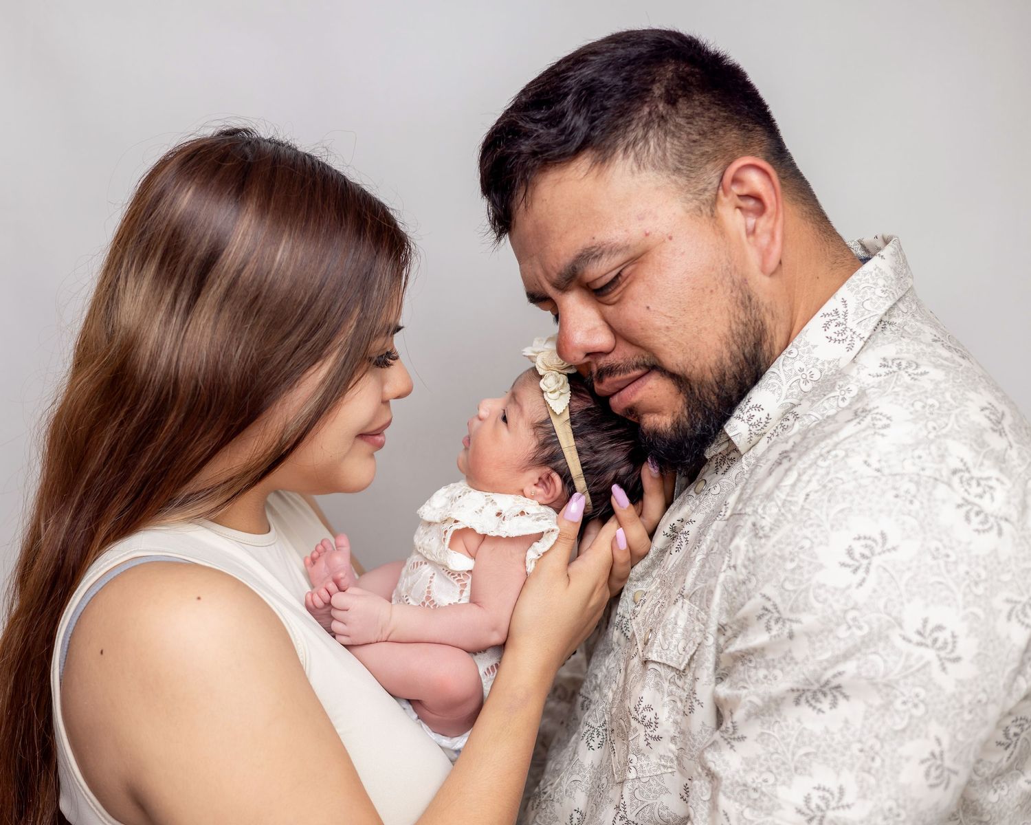 A couple tenderly gazes at their newborn baby during a professional studio portrait session.