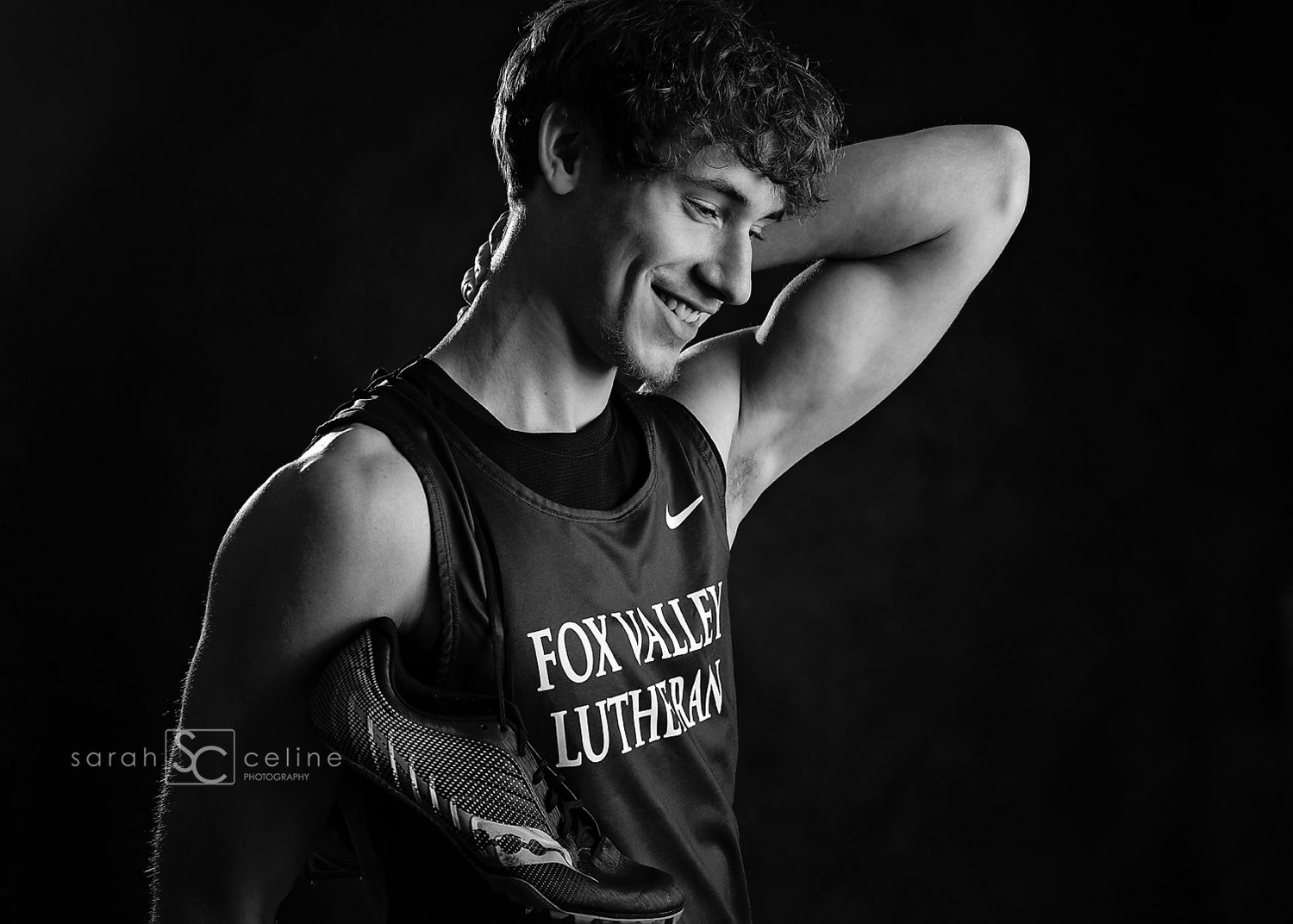 Black and white senior portrait of a smiling young man in a Fox Valley Lutheran track jersey posing confidently.