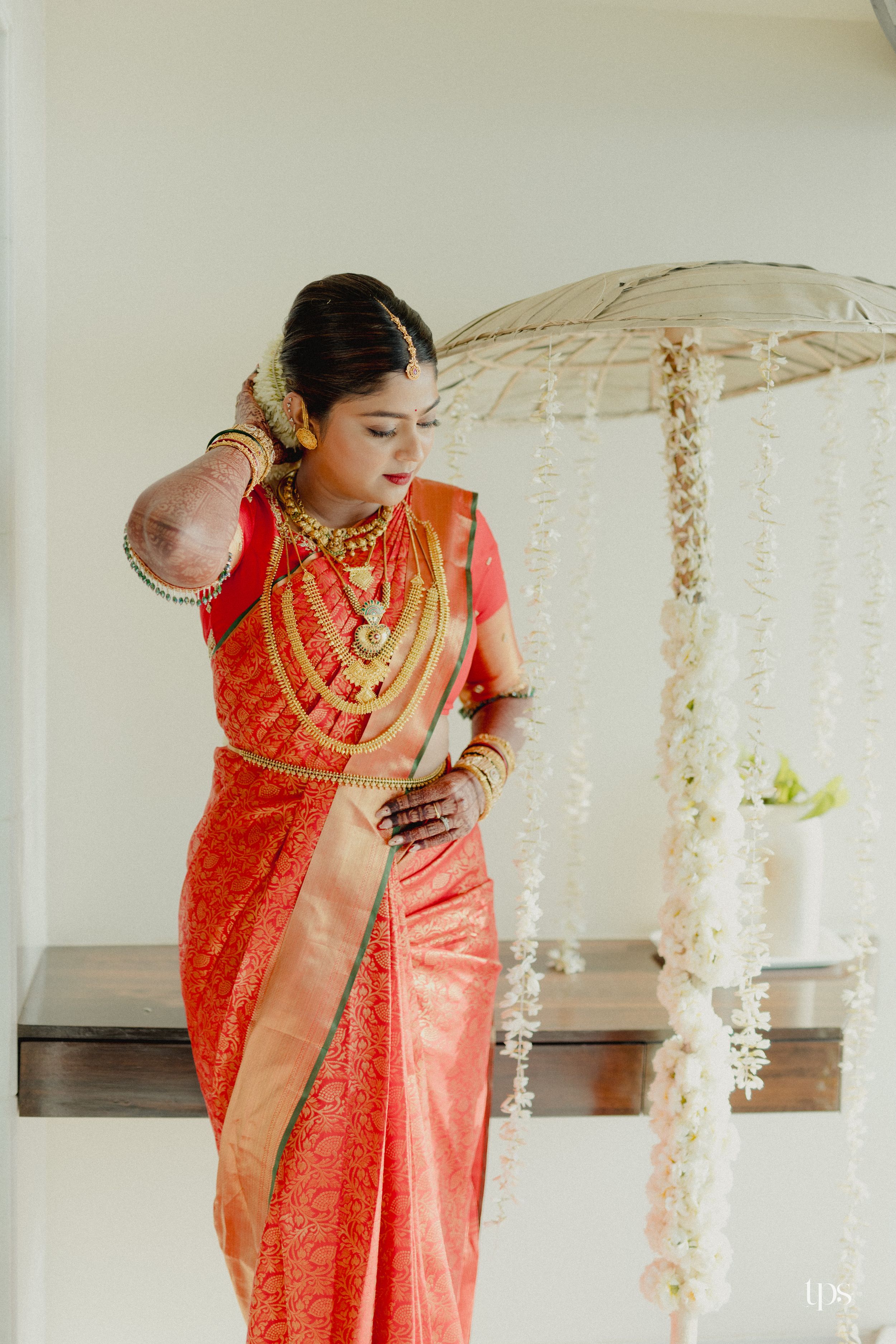 Bride in red Kanjivaram silk saree with gold jewelry and floral decorations at a South Indian wedding.