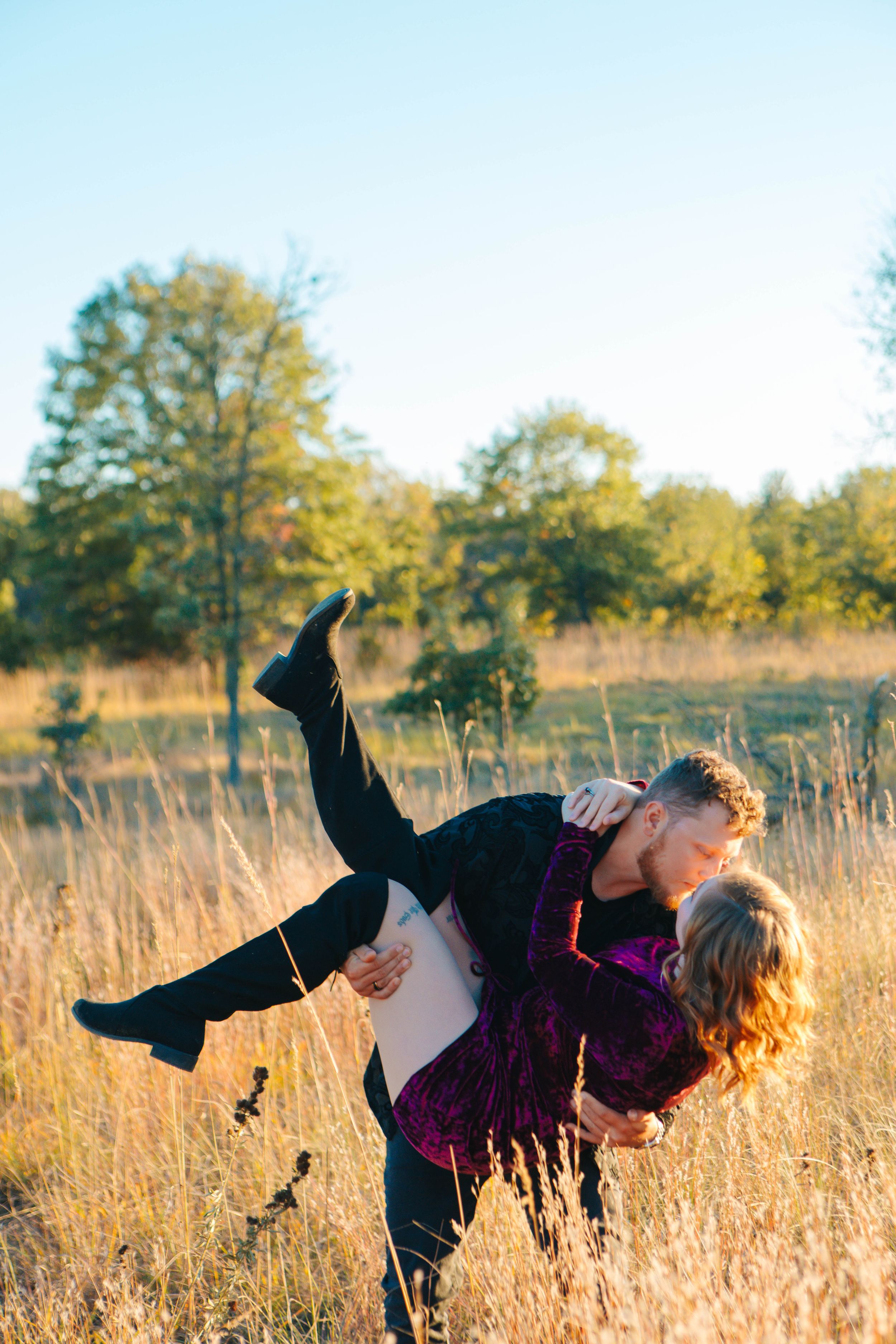 A couple shares a romantic kiss in a golden field, the man lifting the woman in his arms on a sunny autumn day.